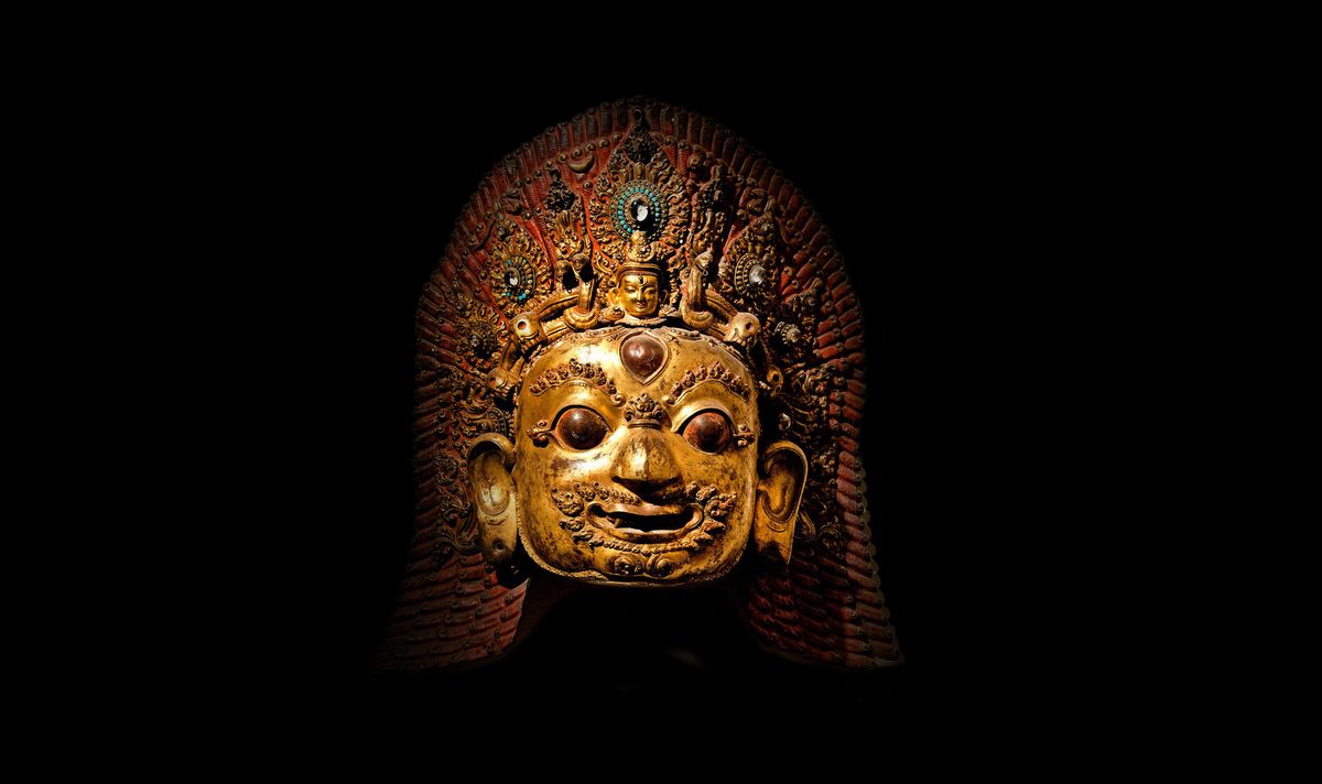 A glowy bronze mask sits in the middle of darkness.